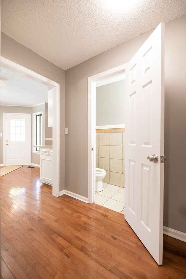 hallway featuring a textured ceiling, light hardwood / wood-style floors, and tile walls