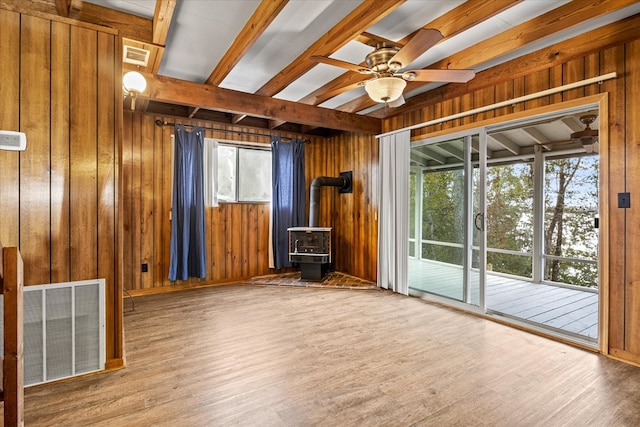 unfurnished room featuring wooden walls, a wood stove, and plenty of natural light