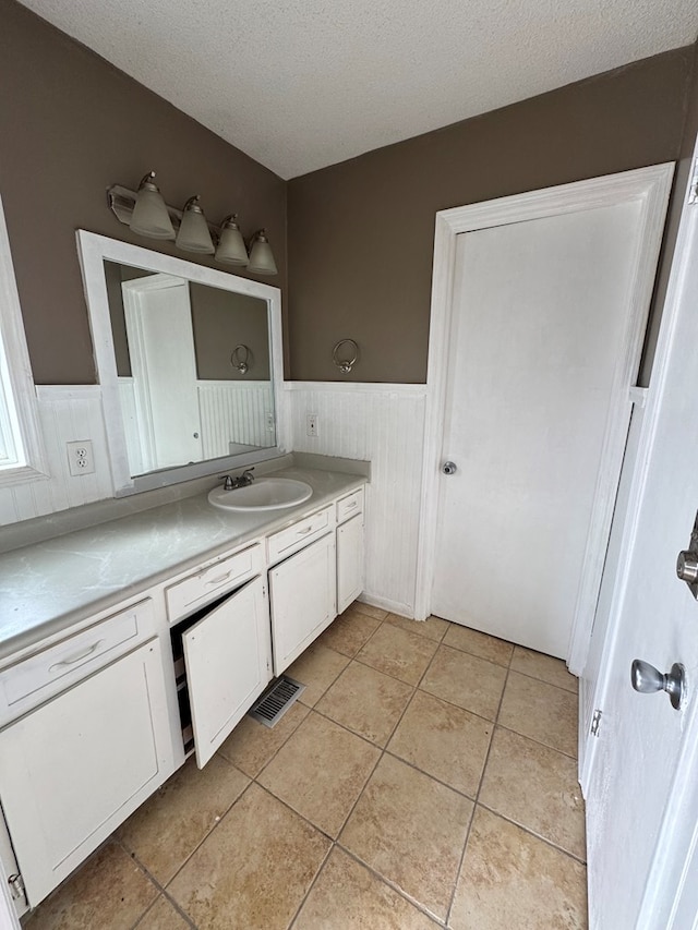 bathroom with a textured ceiling, wooden walls, tile patterned floors, and vanity