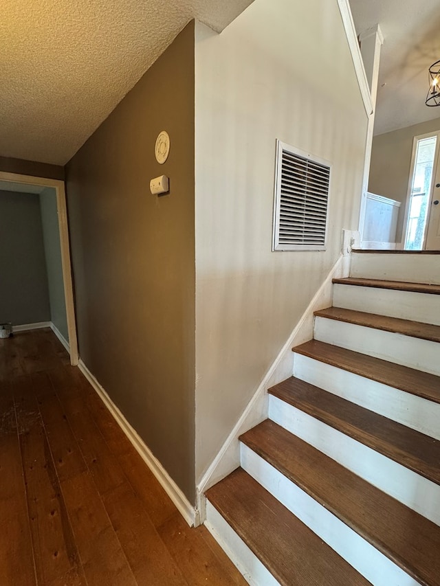 stairway featuring a textured ceiling, hardwood / wood-style floors, and an inviting chandelier