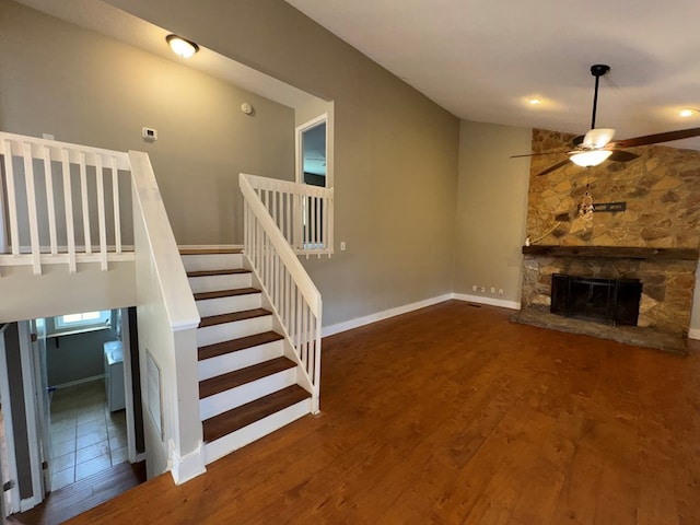 unfurnished living room with ceiling fan, dark hardwood / wood-style flooring, a stone fireplace, and lofted ceiling