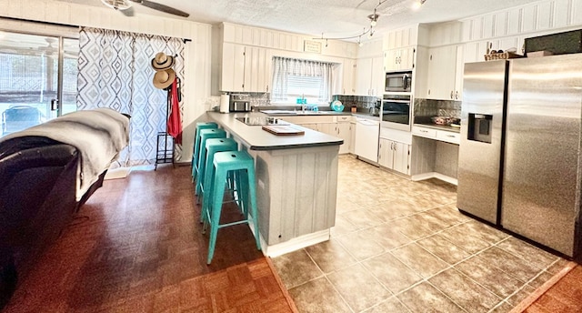 kitchen with kitchen peninsula, appliances with stainless steel finishes, a textured ceiling, white cabinetry, and a breakfast bar area