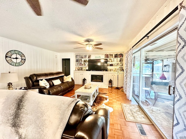 living room featuring wood walls, built in features, a textured ceiling, and light parquet floors