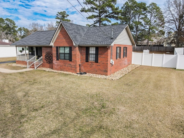 exterior space featuring covered porch, brick siding, a lawn, and a shingled roof