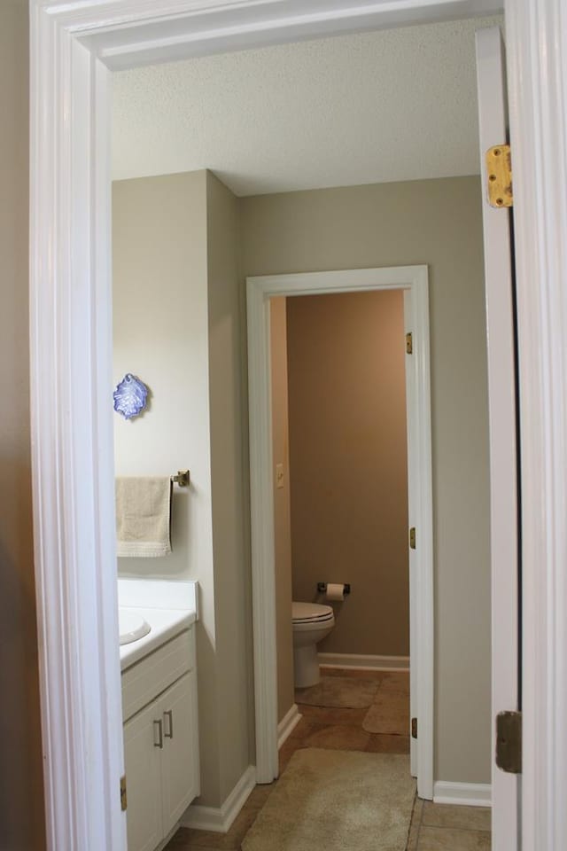 half bath with toilet, baseboards, and vanity