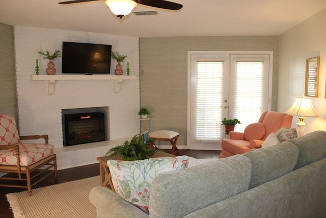 living area with visible vents, ceiling fan, wood finished floors, french doors, and a brick fireplace