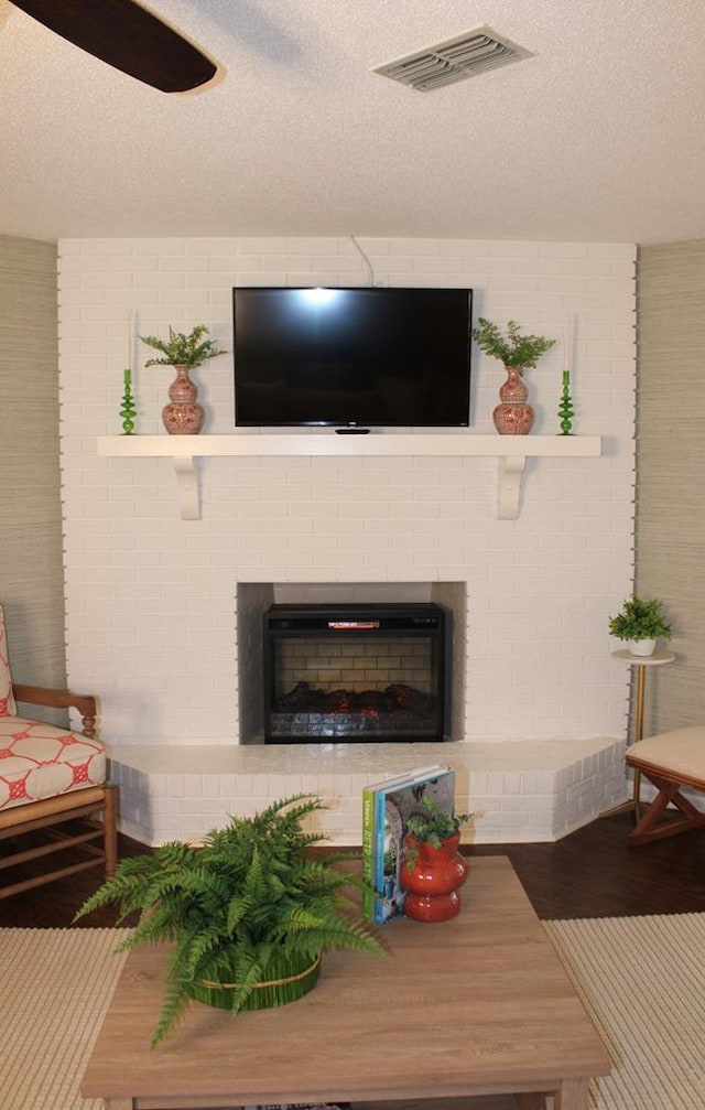 living room with a brick fireplace, visible vents, a textured ceiling, and wood finished floors