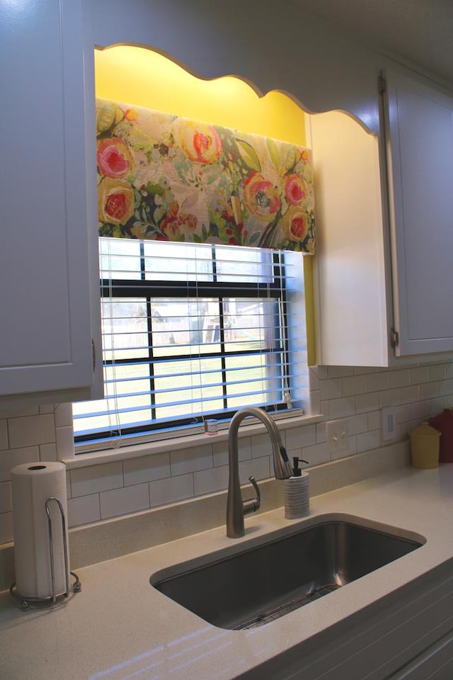 kitchen featuring light countertops, backsplash, a sink, and white cabinetry