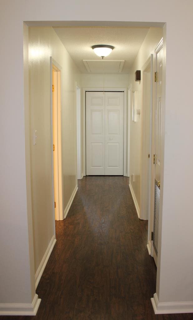 hall featuring dark wood-style flooring, attic access, and baseboards