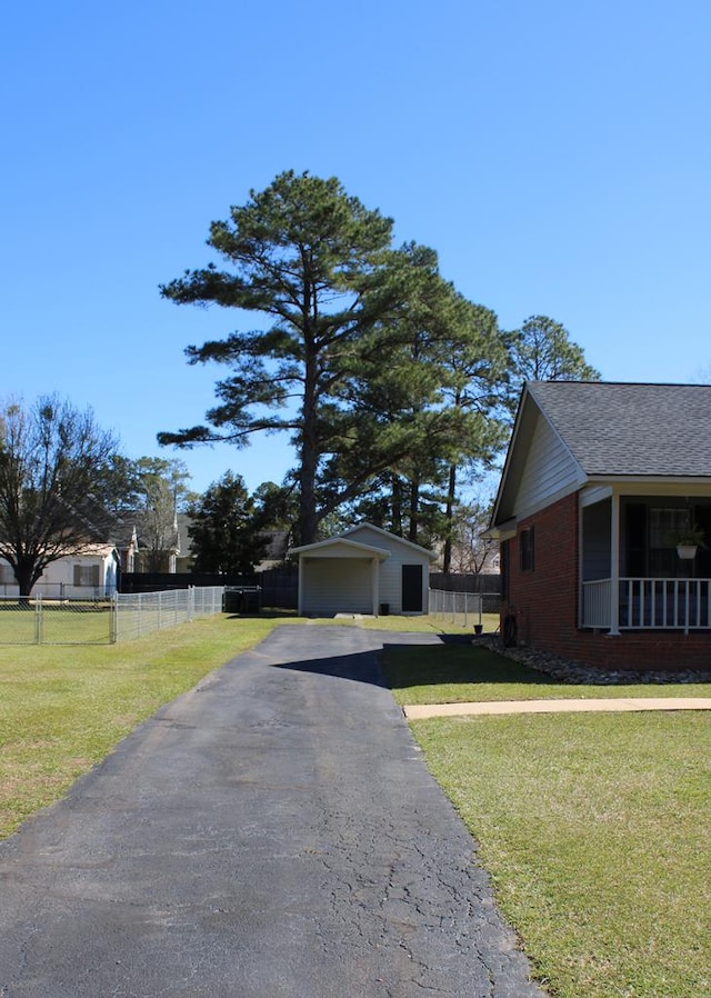 view of side of property with a shingled roof, fence, a lawn, and an outbuilding