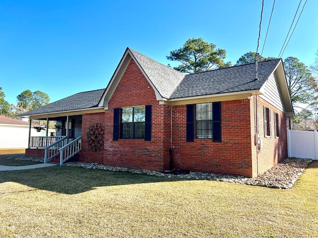 view of front facade featuring a shingled roof, a front yard, brick siding, and a porch