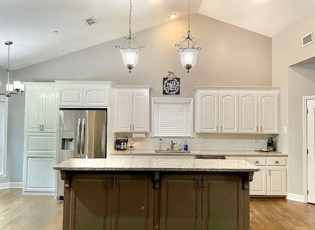 kitchen featuring white cabinetry, a center island, tasteful backsplash, light stone counters, and light wood-type flooring