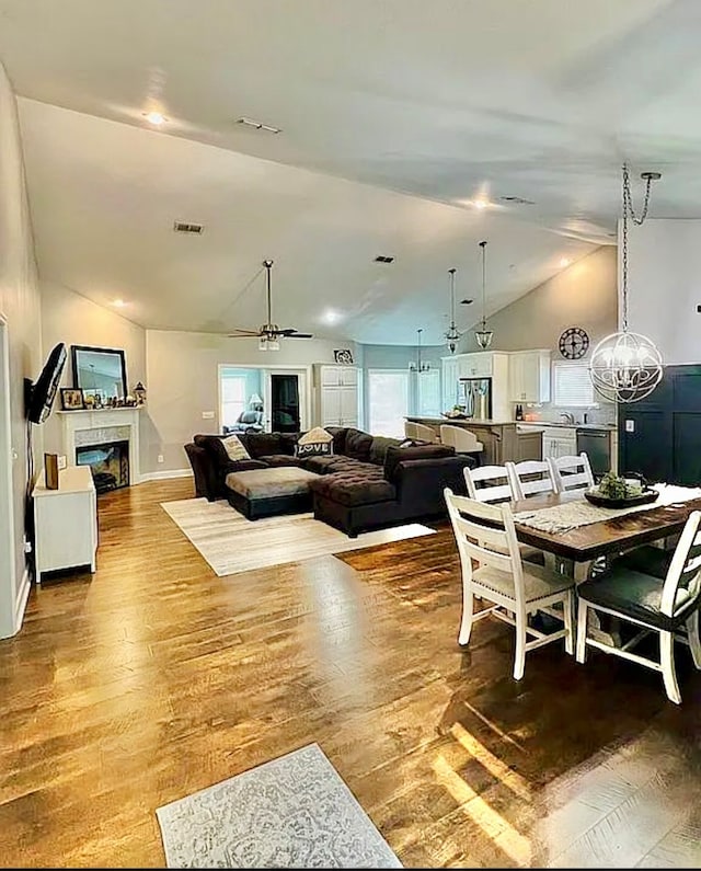 dining room featuring ceiling fan with notable chandelier, wood-type flooring, and lofted ceiling