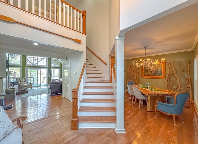 staircase with decorative columns, hardwood / wood-style floors, a chandelier, and ornamental molding