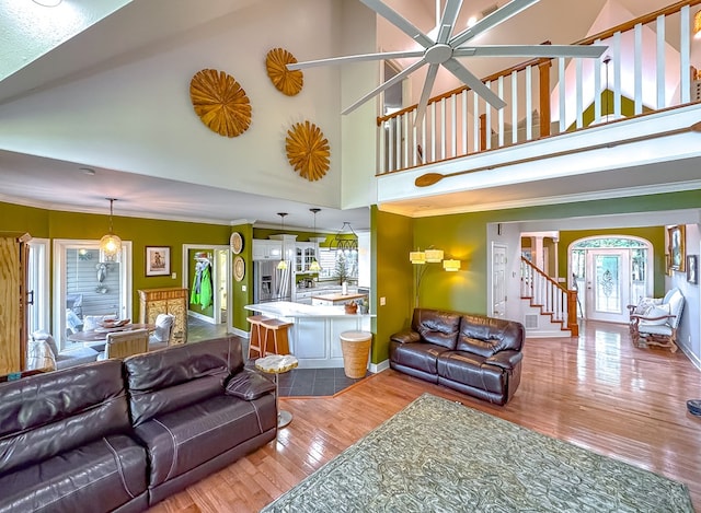 living room featuring wood-type flooring, a towering ceiling, ceiling fan, and ornamental molding