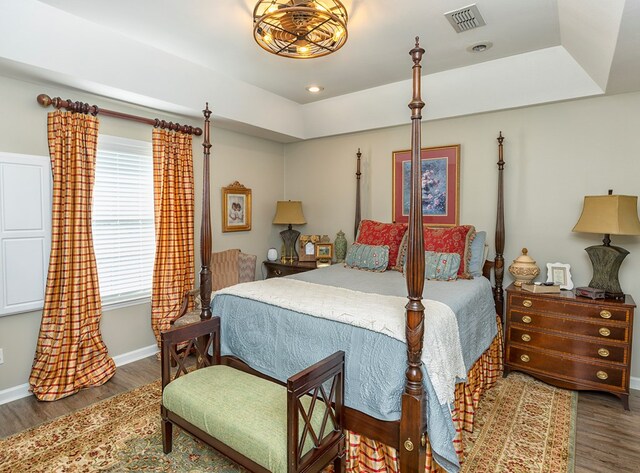 bedroom featuring baseboards, a tray ceiling, visible vents, and wood finished floors