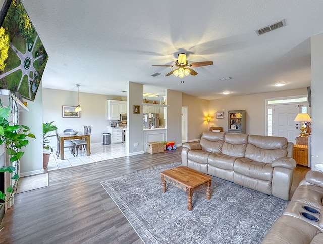 living room featuring light wood-type flooring, ceiling fan, and a textured ceiling