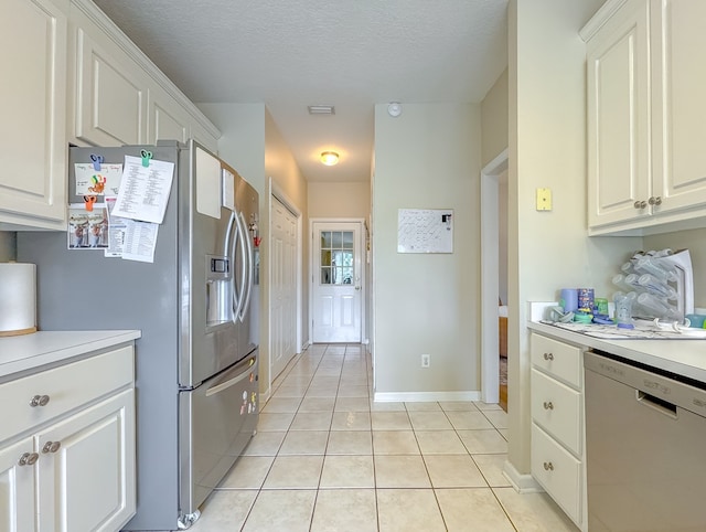 kitchen with appliances with stainless steel finishes, white cabinetry, light tile patterned floors, and a textured ceiling