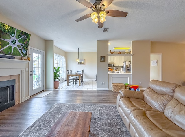 living room featuring hardwood / wood-style flooring, ceiling fan, a textured ceiling, and a tiled fireplace