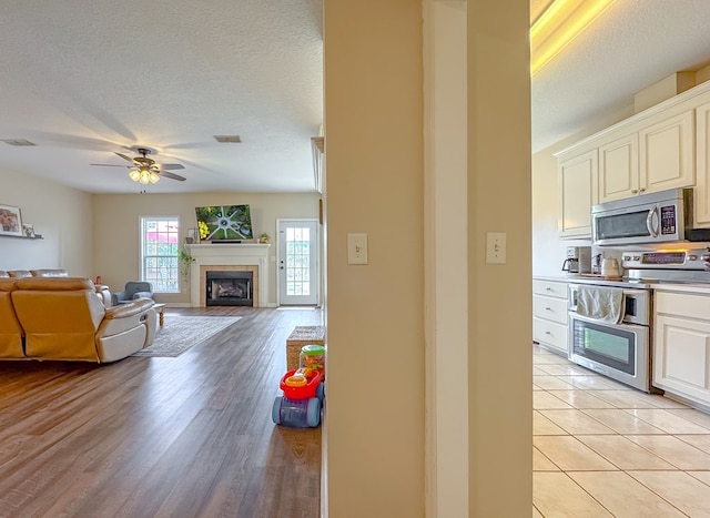 interior space featuring appliances with stainless steel finishes, light tile patterned floors, a textured ceiling, a tile fireplace, and ceiling fan