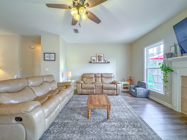 living room with ceiling fan, dark hardwood / wood-style floors, a textured ceiling, and a tiled fireplace