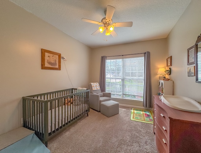 carpeted bedroom featuring a textured ceiling, ceiling fan, and a nursery area