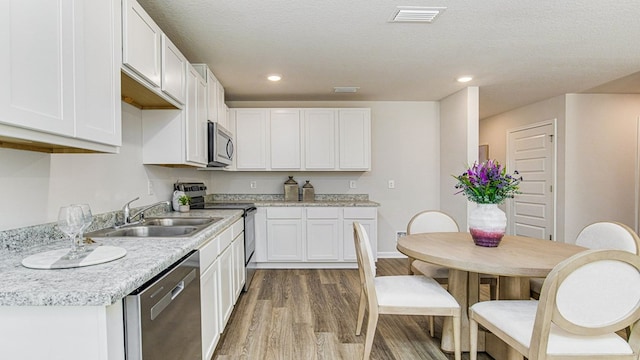 kitchen featuring sink, a textured ceiling, appliances with stainless steel finishes, white cabinetry, and wood-type flooring