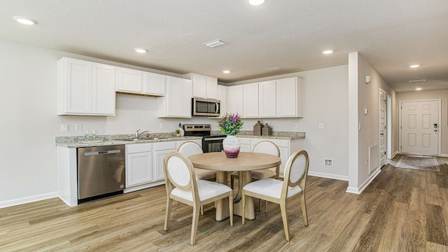 kitchen with a textured ceiling, light wood-type flooring, white cabinetry, and stainless steel appliances