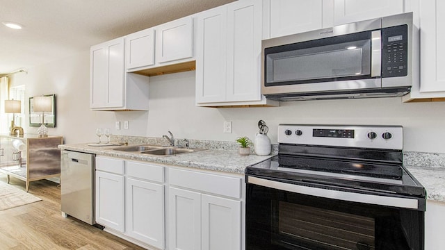 kitchen with sink, light stone countertops, light wood-type flooring, white cabinetry, and stainless steel appliances