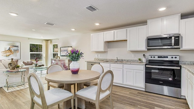 kitchen with light wood-type flooring, a textured ceiling, stainless steel appliances, sink, and white cabinetry