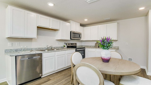 kitchen with appliances with stainless steel finishes, light hardwood / wood-style flooring, white cabinetry, and sink