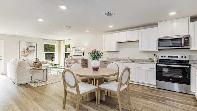 kitchen with sink, stainless steel appliances, white cabinetry, and light hardwood / wood-style flooring