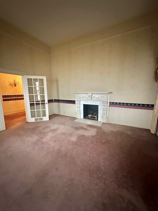 unfurnished living room with a fireplace with flush hearth, french doors, and carpet flooring