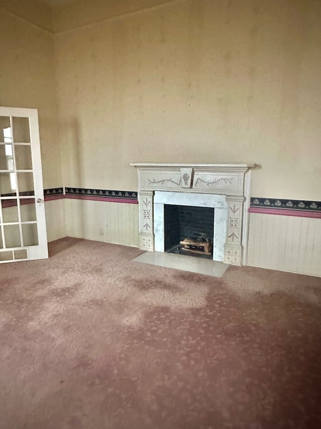 unfurnished living room featuring a wainscoted wall, a fireplace, visible vents, and carpet flooring