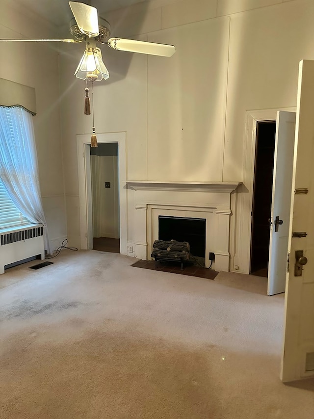 unfurnished living room featuring ceiling fan, a high ceiling, a fireplace with flush hearth, radiator heating unit, and carpet