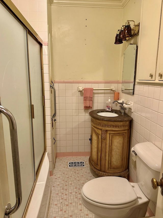 bathroom featuring tile walls, toilet, wainscoting, combined bath / shower with glass door, and vanity