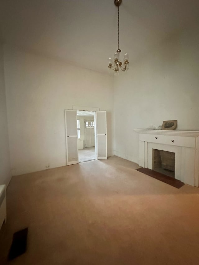 unfurnished living room with a towering ceiling, an inviting chandelier, a fireplace with flush hearth, and light colored carpet