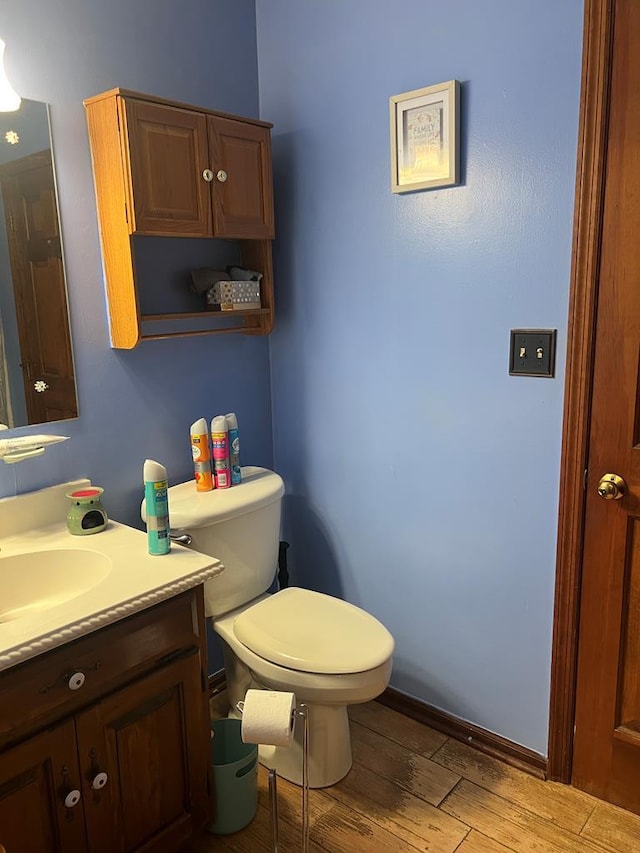 bathroom with vanity, toilet, wood finished floors, and baseboards