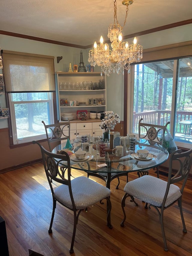 dining area with wood finished floors, a notable chandelier, a healthy amount of sunlight, and ornamental molding