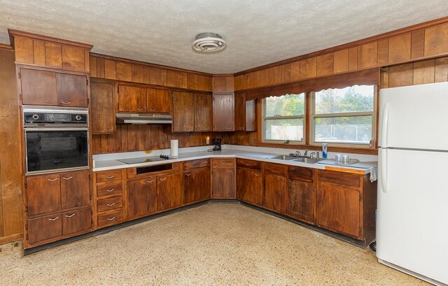 kitchen featuring sink, wooden walls, a textured ceiling, and black appliances