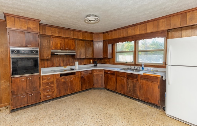 kitchen featuring sink, wooden walls, a textured ceiling, and black appliances