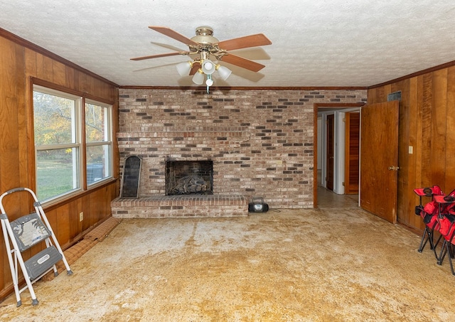 unfurnished living room with a textured ceiling, ornamental molding, ceiling fan, a brick fireplace, and wood walls