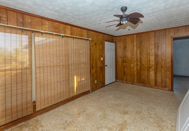 spare room with ceiling fan, ornamental molding, wood walls, and a textured ceiling