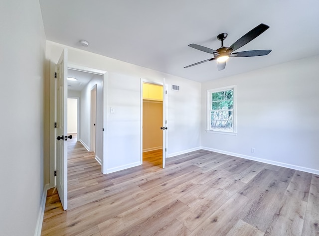 unfurnished bedroom featuring a walk in closet, a closet, ceiling fan, and light wood-type flooring