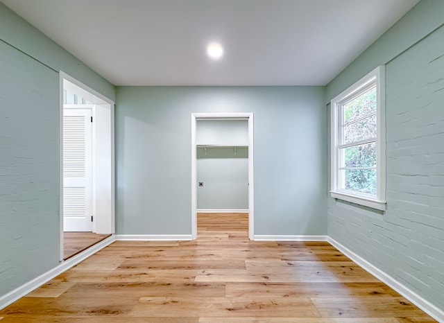 spare room featuring brick wall and light hardwood / wood-style floors