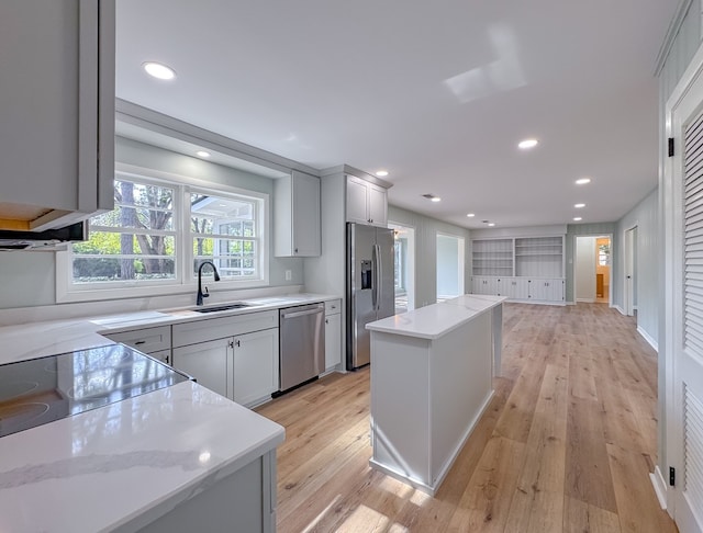 kitchen featuring light stone countertops, a center island, light hardwood / wood-style floors, appliances with stainless steel finishes, and sink