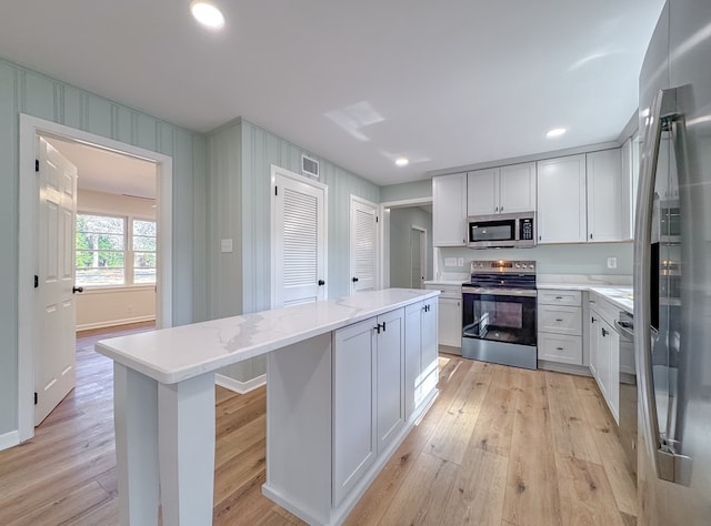 kitchen featuring appliances with stainless steel finishes, light hardwood / wood-style floors, a center island, light stone counters, and white cabinets