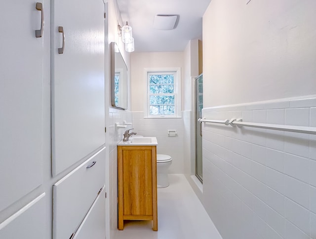 bathroom with toilet, a shower with door, vanity, and tile walls