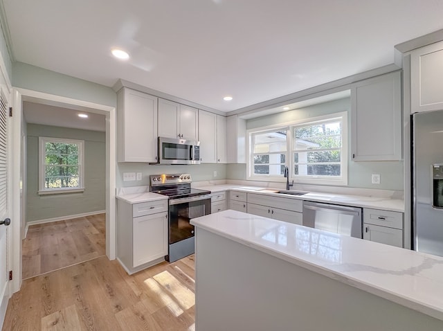 kitchen with light hardwood / wood-style floors, stainless steel appliances, light stone countertops, sink, and white cabinetry