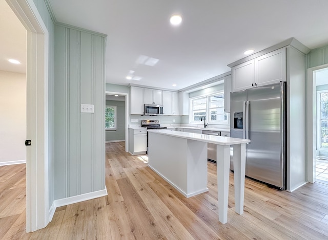 kitchen with light hardwood / wood-style floors, a kitchen bar, a kitchen island, appliances with stainless steel finishes, and sink